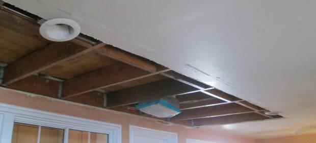 Ceiling with the drywall opened up, exposing the joists and plywood subfloor above.